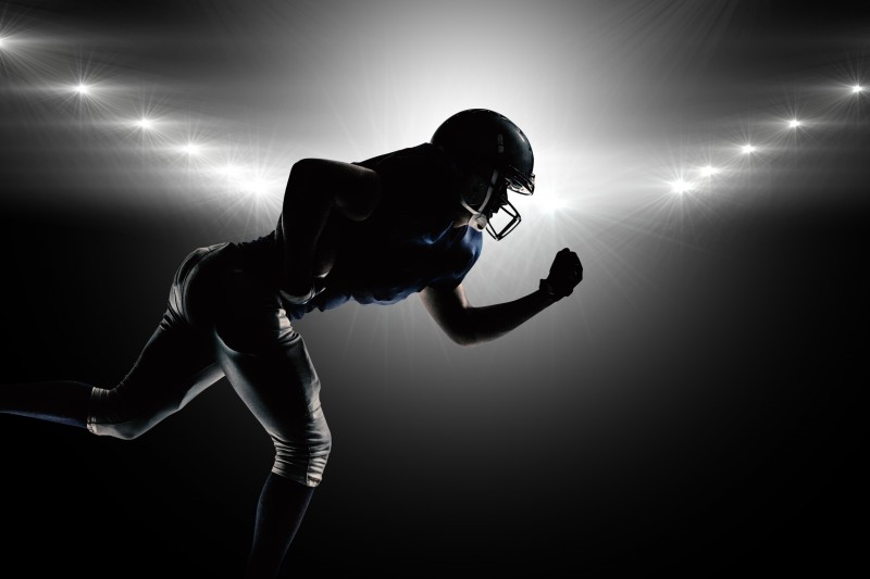 Silhouette American football player running against spotlight