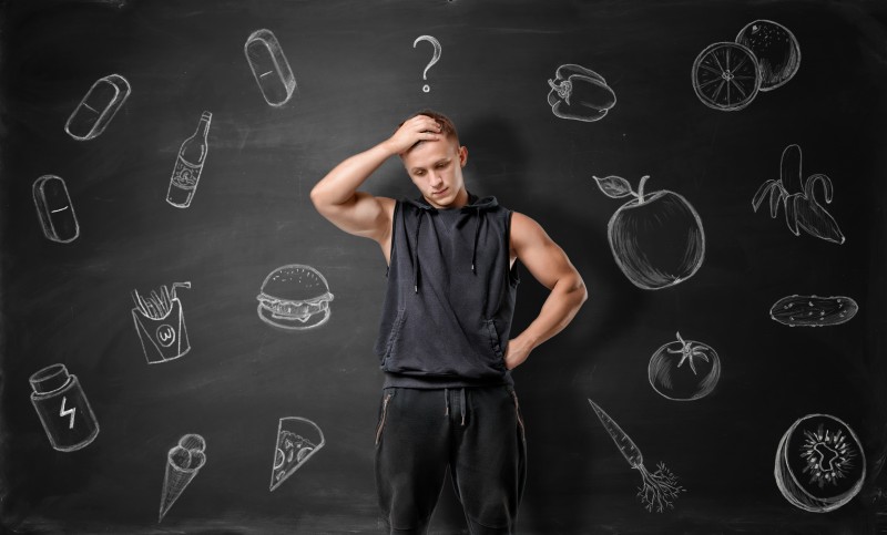 Muscled young man pondering on what to choose: junk or healthy food