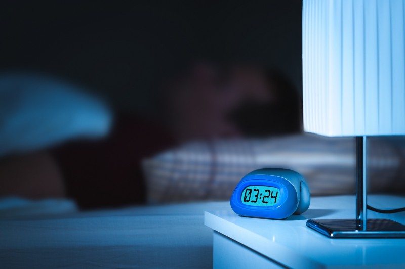 Man sleeping in bed. Digital alarm clock on nightstand in bedroo